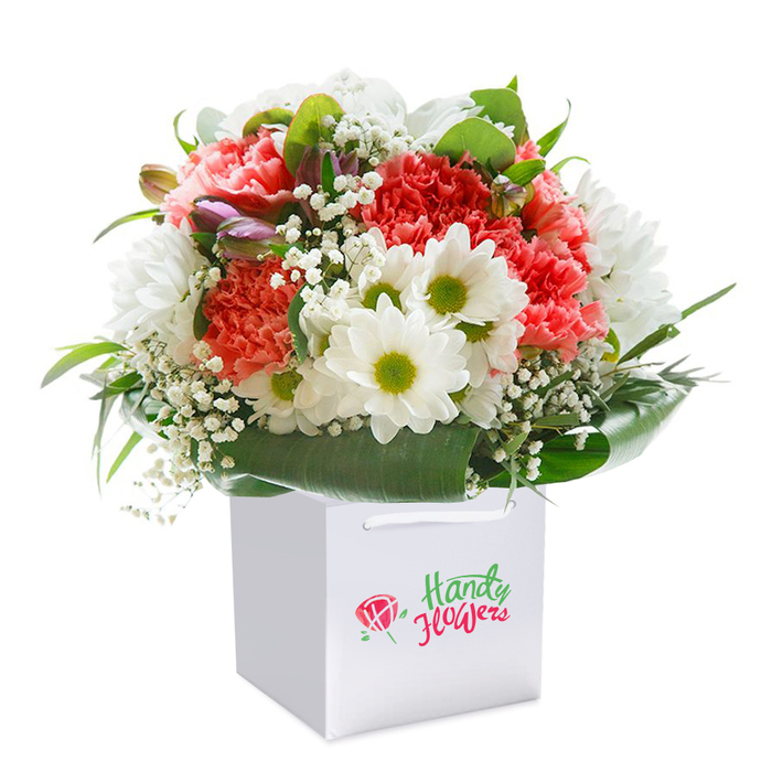 Presented upright in a sophisticated square white gift bag, this beautifully curated bouquet offers an expressive showcase of florist craftsmanship, as seen in Catford's finest shops. Soft-hued coral-pink and radiant red carnations dominate the arrangement with their lush, ruffled petals, their vibrancy reflected in the animated street life of Catford itself. White daisies with lime-green centers emerge in gentle contrast, capturing the uplifting mood of a stroll through nearby Riverview Walk. Airy sprigs of delicate baby's breath lend a sense of movement and lightness, their tiny white blossoms delicately filling the spaces between statement flowers. Enriching the palette, a handful of unopened blooms edged in soft purple peek subtly from the left, introducing visual intrigue and a whisper of the new nearby blooms seen every spring. The foundation of deep, glossy green leaves forms a tailored natural collar, showcasing a rich, harmonious structure wrapped around the base-mirroring the welcoming green spaces of Catford. The arrangement bursts confidently with rounded fullness, every stem strategically placed for optimal texture, colour, and balance. The white gift bag stands as a symbol of thoughtful giving, its smooth, sturdy handles ensuring effortless carrying for same-day delivery to homes near the South Circular or Catford station. Captured against an immaculate white background, every petal and ribbon is revealed in its truest tone. This elegant display embodies quality, freshness, and a sense of abundance-perfect for delivering joy for birthdays, anniversaries, or simply bringing sunshine into a Catford household.