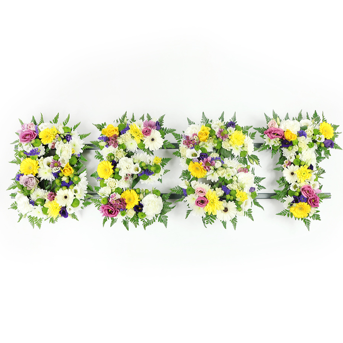 Centered horizontally in crisp studio light, this bespoke floral tribute spells BEST with four independently crafted letters, each densely packed with fresh, tactile blooms and lush greenery. White, chrysanthemum-like flowers form soft, pillowy backbones across the letters, their layered petals creating a calm, luminous base. Bright yellow roses and gerberas provide joyful, lemon-tinged highlights that feel warm and consoling, while clusters of purple and mauve lisianthus or similar small blooms introduce elegant contrast and a graceful, contemplative cadence. Vivid fuchsia and magenta spray roses or carnations are woven throughout to lift the composition with cheerful punctuation, and tiny green-and-white filler blooms add fine detail and a light, airy texture between the larger heads. Fern fronds border each letter generously, their deep green, serrated edges giving a natural silhouette and a soft, living frame that keeps the focus on the flowers. Where the blooms are less dense you can see the dark green or grey support bars that give the letters structural integrity, notably along the E's horizontal bar and the T's cross; these practical elements are thoughtfully concealed by floral layering. The even, front-facing illumination emphasizes petal texture and colour fidelity, and the overall effect is both handcrafted and dignified - suitable for memorials, commemorations or special tributes where one wants to honour someone as the best. Available for thoughtful local delivery across Catford and nearby Lewisham neighbourhoods, this design reads as both a statement of love and a skilled piece of floristry.