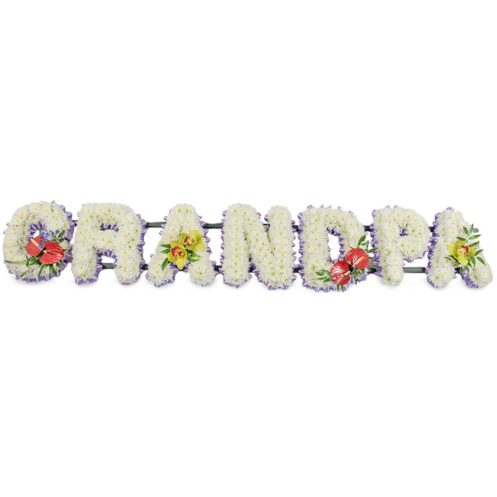 A refined funeral flower tribute forms the word GRANDPA in large block capitals, laid out in a continuous line against a neutral white background, as if ready to rest on top of a coffin during a service in Catford or to be placed at graveside afterwards. Each letter is constructed on a sturdy dark green frame and then completely covered with tightly massed white chrysanthemums, so that the overall impression is one of smooth, soft, snow-like texture. The chrysanthemums' many petals catch the light, giving the surface a gentle sheen, while the rounded flower heads sit snugly together, signifying unity and calm. Around the base of every letter runs a border of pale lavender ribbon, just visible as a cool halo of colour that gently outlines each shape and adds a subtle, comforting hint of purple without disturbing the purity of the white.
Colourful focal sprays have been carefully placed to personalise the design. On the far left, the letter G carries a striking arrangement of deep red anthuriums, their glossy, heart-shaped spathes and prominent yellow spadices nestled among dark green foliage and possibly a few tiny purple filler flowers, creating a vivid point of remembrance. Moving along, the first A is decorated with elegant yellow-green orchids, their graceful blooms and fresh foliage suggesting vitality and the enduring bond between generations. Near the centre-right, the letter D echoes the G with a second cluster of rich red anthuriums and greenery, balancing the composition. Finally, the end A on the right repeats the lime-toned orchids, closing the tribute with the same gentle brightness that began it. This handcrafted piece, the kind a family might order from a trusted Catford florist, offers a dignified and deeply affectionate farewell to a grandfather, capturing memories of local life-from quiet conversations at home to strolls around Ladywell Fields-in a carefully considered blend of colour and texture.