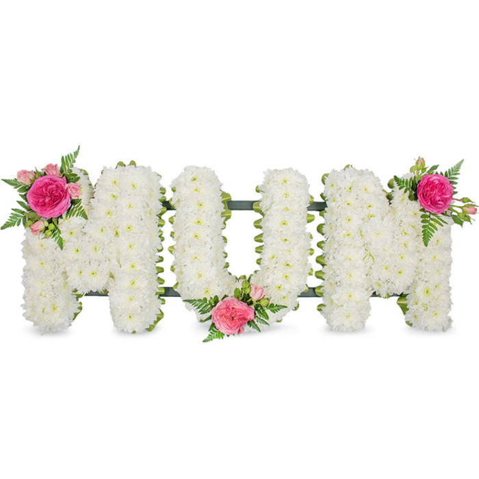 A deeply touching floral tribute spells out MUM in generous capital letters, meticulously crafted so that each stroke is completely filled with tight clusters of white chrysanthemums. The flowers are arranged so densely that no gaps are visible, giving every letter a smooth, cushion-soft surface and a refined, traditional look often favoured for heartfelt funeral tributes in Catford. The chrysanthemums' bright white petals reflect the surrounding light, making the letters seem to glow gently against the plain white backdrop. Beneath the flowers, a sturdy dark green frame and coordinating ribbon subtly edge the base of each letter, providing structure and a clean outline, while adding a calm, natural contrast. Carefully placed along the word are three matching clusters of vivid pink blooms. At the upper left of the first M, a full, ruffled fuchsia rose sits at the centre of a small spray of lighter pink roses and buds, all softened by airy fern foliage. In the dip of the U, another cluster of fuchsia and blush-pink roses rests low, almost as if cradling the central letter. The second M is crowned on its upper right with the final grouping of these same pink tones, creating a balanced triangle of colour from left to right. The simplicity of white and green, lifted by the romance of pink, makes this MUM arrangement a tender choice for families saying goodbye at local Catford services, expressing love, gratitude, and a peaceful farewell through expertly composed flowers.