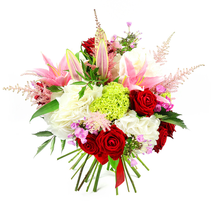 The image presents a richly detailed hand-tied bouquet, photographed against a pure white background so that every colour and texture stands out with clarity. Dominating the composition are several lush crimson roses, their velvety petals layered in tight whorls that give a sense of depth and timeless romance. Interwoven among them are tall, graceful pink lilies; some are fully open, their star-shaped blooms revealing soft inner markings and golden stamens, while others remain partly closed, slender buds hinting at fragrance still to come. Supporting these main flowers, generous heads of ruffled white blossoms form a soft, cushiony base, reminiscent of full carnations or hydrangeas, creating a luxurious foundation that feels almost cloud-like to the eye. Near the centre, a perfectly rounded cluster of lime green dianthus draws attention with its unusual mossy texture and vibrant, almost glowing colour, bringing a fresh, modern edge to the otherwise classic palette. Delicate plumes of pale pink astilbe stretch upwards and outwards, adding a feathery, ethereal quality, as though the bouquet has captured a little of the morning mist that sometimes settles over nearby Mountsfield Park in Catford. Small clusters of fuchsia-pink and lavender filler flowers are tucked between the larger blooms, offering playful flashes of deeper colour and enhancing the sense of abundance. Dark green foliage weaves throughout, the glossy leaves framing the blossoms and grounding the arrangement in nature. At the base, the stems are clearly visible, neatly aligned and tied with an elegant red satin ribbon that emphasises the hand-crafted nature of the piece. The overall impression is of a joyful, opulent bouquet, ideal for romantic gestures, anniversaries, or as a striking centrepiece delivered fresh to homes and businesses across Catford.