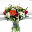 This bouquet is a vibrant celebration of freshness and colour, masterfully arranged in Catford and inspired by the spirited energy of the local community. At the arrangement's center, a dazzling tangerine Gerbera radiates optimism, surrounded by creamy white alstroemeria whose gracefully arching petals evoke swans gliding along nearby Ladywell Fields. Intertwined with these are deep magenta roses, their petals unfolding with lush delicacy, alongside clusters of daisy-like white chrysanthemums that offer a lacy contrast. Hints of pale yellow and soft lavender heighten the bouquet's complexity, while the entire composition is embraced by generous, glossy greenery-broad leaves curl around the base as slender, upright fronds bring a sense of motion. Nestled within a simple clear glass vase, the vivid stems are reflected in fresh water and bathed in gentle daylight, conjuring the impression of a Catford morning alive with possibility. Whether marking a birthday, anniversary, or a heartfelt thank you, this arrangement embodies the joy and renewal found in every corner of Catford, perfect for lighting up homes and hearts across SE6.