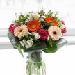 Vivid and inviting, this bouquet evokes the spirit of Catford with an artful gathering of nature's brightest hues. Soft peach gerberas, each petal radiating calm warmth, nestle beside their fiery orange counterparts-together brightening the composition like an early summer dawn. Rich magenta roses spiral gracefully through the arrangement, lending an air of timeless romance and depth, while tufts of pristine white alstroemeria and dainty filler flowers lift the display with gentle lightness. Light pink blooms tease the eye, furthering the sense of abundance that characterizes this bouquet. Surrounding them, a flourish of deep green aspidistra leaves forms a strong, protective base, wrapping the blossoms in luminosity and grace. Slender, pointed leaves and delicate greenery weave throughout, mirroring the lush canopies found in Catford's parks and avenues. Housed in a tall, transparent glass vase, the bouquet's fresh stems are visible, grounding its lively colours with a touch of honest earthiness. The soft, radiant background-suggestive of sun filtering through a kitchen window on Blythe Hill-ensures the flowers remain the radiant focal point. Perfect for celebrating milestones, welcoming friends, or simply sending a thoughtful gesture across SE6, this bouquet encapsulates freshness, beauty, and the welcoming essence of Catford's vibrant community.